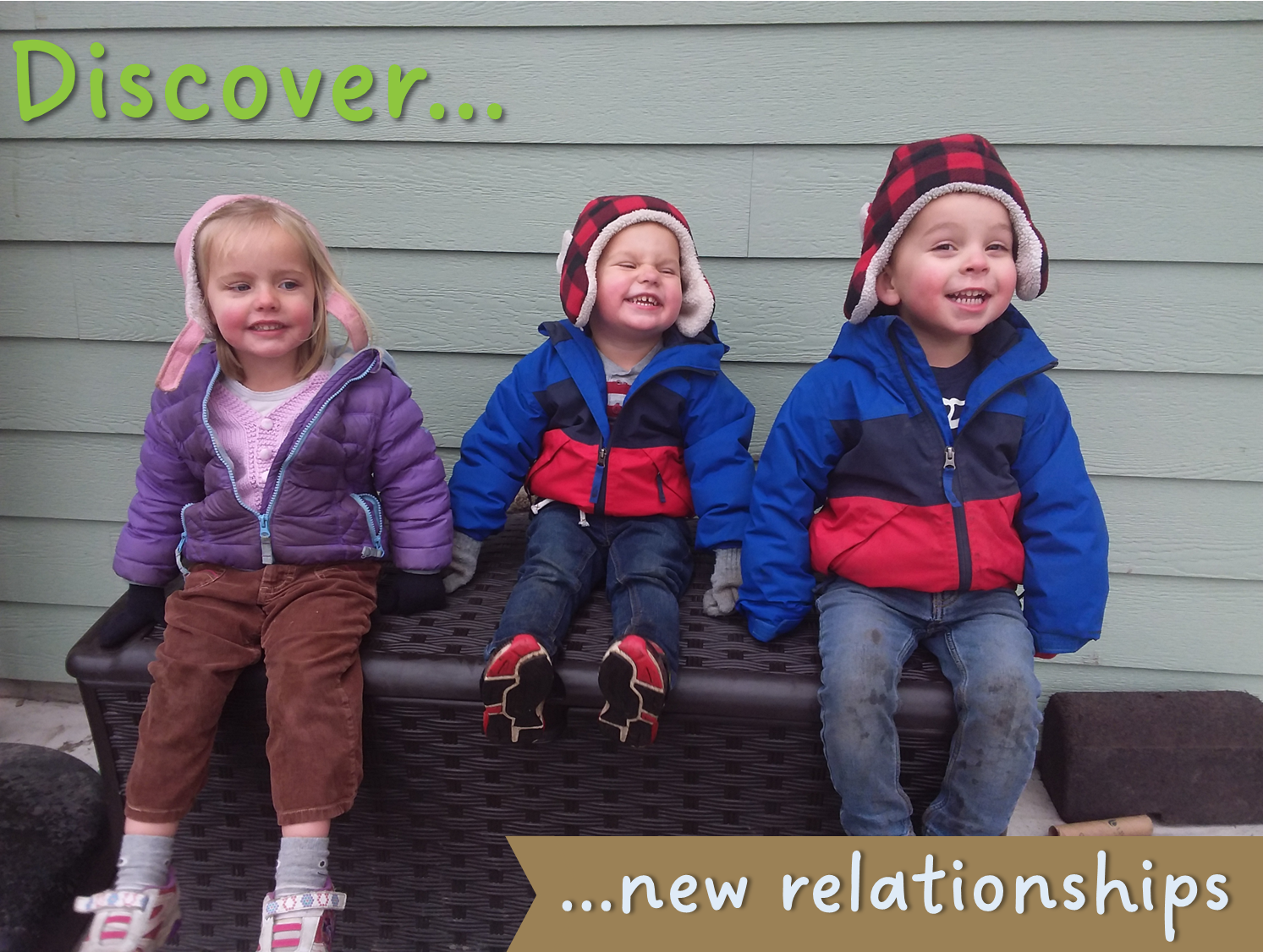 Three young children wearing winter coats sit on a bench outside. The two boys wear matching coats and hats.