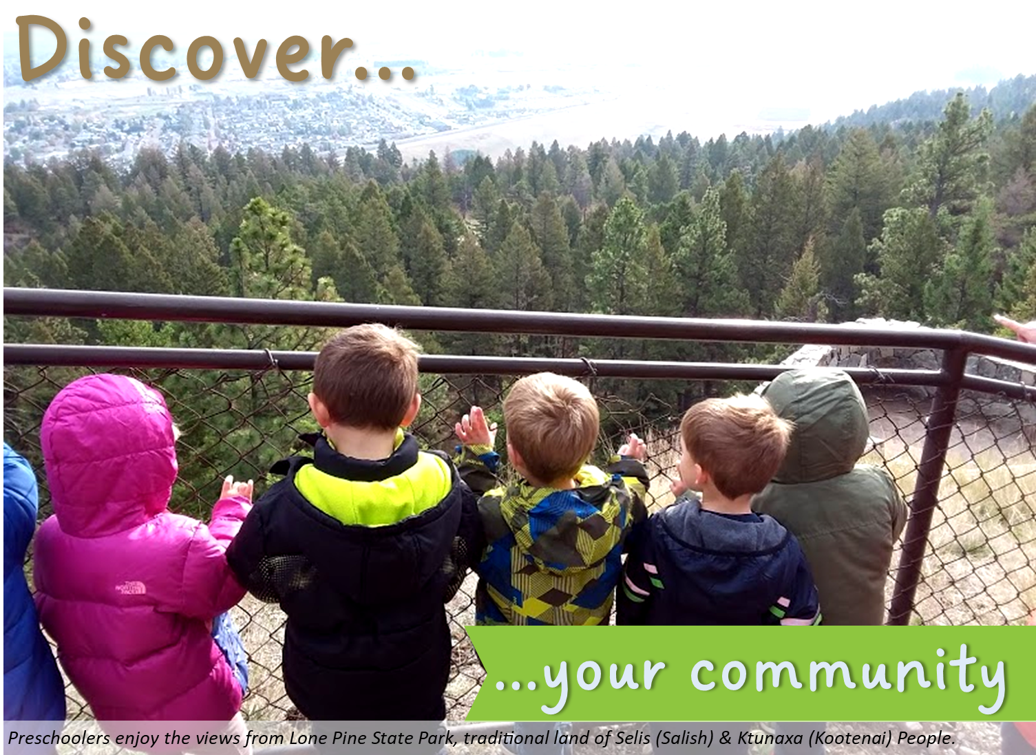 Five preschoolers in coats stand at a chain-link fence, looking over a forest of pine trees and a valley.
